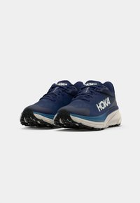 Hoka hardloopschoenen in donkerblauw met grijze accenten, voorzien van een gestructureerde bovenkant, opvallende veters en een robuuste zwarte buitenzool voor grip.