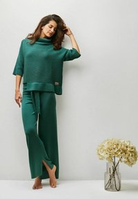 Grüner, gerippter Strickpullover mit hohem Kragen und weiten Ärmeln, kombiniert mit langen, passenden Hosen, die ein Bindeband in der Taille haben.