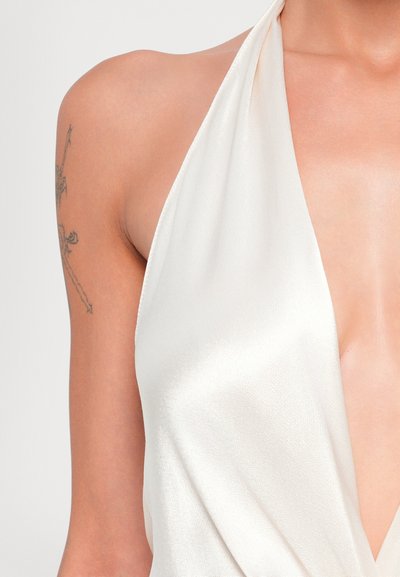 Biely saténový halter top s hlbokým výstrihom, ktorý vystihuje hladkú štruktúru a priliehavý strih. Obsahuje jemný lesk.