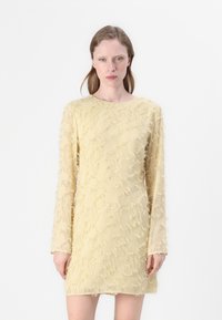 Gelbes Kleid mit langen, durchsichtigen Ärmeln, das ein strukturiertes, ausgefranstes Muster aufweist. Die Silhouette ist figurbetont mit einem runden Ausschnitt.