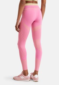 Leggings roses avec un motif texturé composé de lignes diagonales et de points, accompagnés de baskets roses et d'une ceinture légère verte.