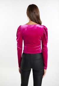 Tætsiddende, langærmet top i lys pink velour med puffede skuldrer, parret med sorte højtaljede bukser med baglommer.