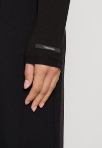 Schwarzes Langarmkleidungsstück mit figurbetonter Passform. Verfügt über ein kleines Calvin Klein-Logoetikett am Ärmel. Glatte, elastische Stoffoberfläche.