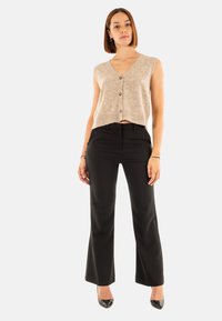 Cardigan sin mangas beige con escote en V y botones en la parte frontal, combinado con pantalones de campana negros y tacones de charol negros. Textura suave.