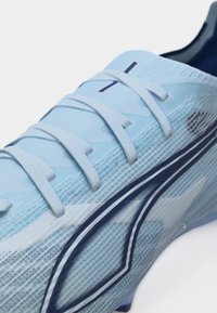 Light blue soccer cleat with white laces and dark blue design accent, showing detailed texture on upper material.