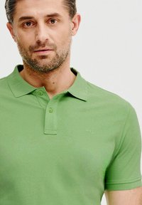 Zielona koszulka polo z miękkiego, gładkiego materiału. Posiada klasyczny kołnierzyk, zapięcie na dwa guziki oraz subtelne logo na klatce piersiowej.