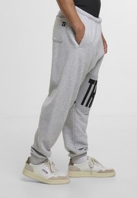 Sivé tepláky s voľným strihom, so bočnými vreckami, rebrovanými manžetami a veľkou čiernou grafikou na ľavej nohe.