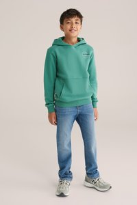 Grön sweatshirt med huva, framficka och ribbade mudd, i kombination med ljusblå jeans och grå sneakers med svarta accenter.