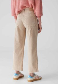 Pantalon beige clair taille haute à coupe large, avec deux poches à l'arrière, porté avec des baskets grises et bleues. Le pull a une coupe ample.