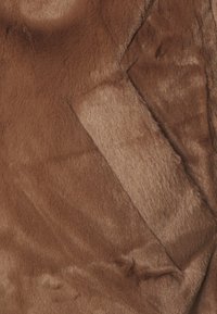 Tejido de imitación de piel suave en marrón, con una costura visible y borde doblado que crea una textura en capas.