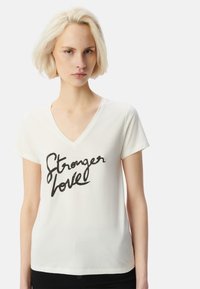 Camiseta de algodón blanca con cuello en V, mangas cortas y un estampado en cursiva negra que dice "Stronger love" en el pecho.