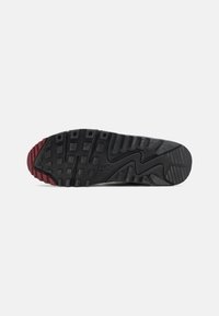 Semelle de sneaker noire et bordeaux avec un caoutchouc texturé, des motifs de traction et un logo Nike bien en vue. Conçu pour l'adhérence et la durabilité.