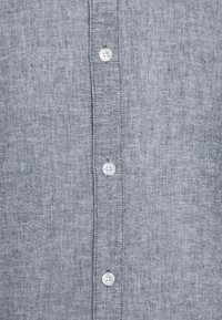 Light gray linen shirt featuring a button-up front with white buttons and a textured fabric. The design is classic with a clean, simple finish.