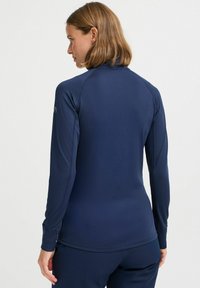 Sötétkék hosszú ujjú sportpóló sima anyagból, magas gallérral és testhez simuló mandzsettákkal, diszkrét varrási részletekkel.