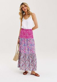 Maxi sukně s vrstveným designem, zdobená růžovými, fialovými a modrými paisley vzory. Spárovaná s bílým tílkem a hnědými sandály.