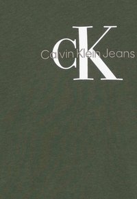 Oliwkowa koszulka z bawełny o gładkiej fakturze, z dużym białym logo "CK" oraz napisem "Calvin Klein Jeans".