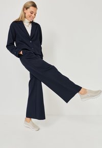 Marineblauer Nadelstreifen-Blazer mit zwei Knöpfen und passender weiter Hose, kombiniert mit hellbeigen Slippern. Glatter Stoff und lockere Passform.