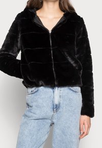 Chaqueta negra con cremallera de piel sintética y capucha, con un diseño acolchado. Combinada con vaqueros de mezclilla azul claro de talle alto.