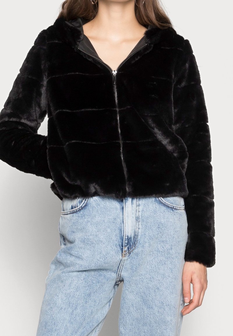 Chaqueta negra con cremallera de piel sintética y capucha, con un diseño acolchado. Combinada con vaqueros de mezclilla azul claro de talle alto.