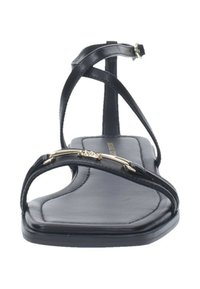 Sandalia de cuero negro con tiras finas, que presenta un detalle decorativo en dorado. La suela es plana con una textura suave y un diseño minimalista.