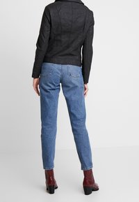 Sort faux læderjakke med tætsiddende design og skulderdetaljer, parret med lyseblå højtaljede jeans og bordeaux hæl støvler.