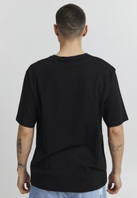 T-shirt di cotone nero con vestibilità rilassata, maniche corte e scollatura a costine; presenta un'etichetta con logo visibile all'orlo.