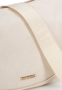 Borsa color crema realizzata in pelle sintetica testurizzata, caratterizzata da una placca con logo dorato e una tracolla beige con motivo.