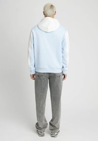 Hoodie bleu clair avec des manches blanches, en tissu doux, coupe décontractée. Associé à un pantalon gris ample et des baskets, vu de dos.