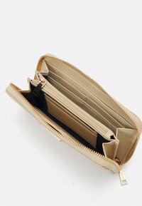 Portafoglio beige con zip perimetrale, numerosi scomparti per carte, un comparto centrale, zip in tono oro e rivestimento interno nero. Texture liscia.