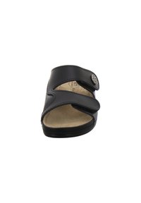 Schwarze Slipper-Sandale aus synthetischem Leder mit zwei verstellbaren Riemen. Polsterung im Fußbett und ein runder dekorativer Knopf an der Seite.