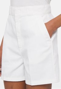 Shorts bianchi in cotone con vita alta, davanti piatto, tasche laterali e un design strutturato. Texture liscia con un aspetto pulito e minimalista.