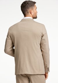 Beige colbert met een gestructureerde stof, een enkele uitsparing aan de achterkant en driedubbele knopen bij de mouwen. Strakke, op maat gemaakte lijnen die de structuur benadrukken.