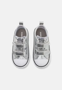 Strieborné látkové tenisky s suchými zipsami, čiernymi akcentmi a bielymi gumovými podrážkami. Textúrovaná vnútorná stielka zobrazuje branding "Converse All Star".