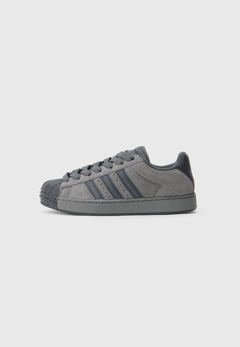 Gray suede sneakers with a rubber shell toe, featuring three dark gray stripes, textured laces, and a padded ankle collar.