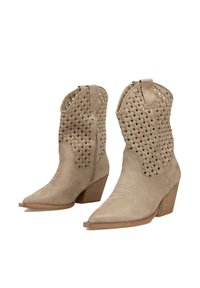 Botas de vaquero de ante beige con parte superior tejida, puntas afiladas y tacón de madera apilada. Cuenta con detalles de costura en el panel del pie.