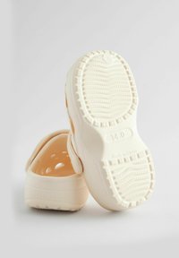 Zuecos de color beige claro hechos de material flexible, con una suela texturizada, orificios de ventilación y una correa trasera para un ajuste seguro. Talla 14.0.