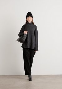 Pull à col roulé gris surdimensionné avec ourlet en côte, associé à un pantalon large noir et des bottines à talons grises. Accessoire : sac à main noir.