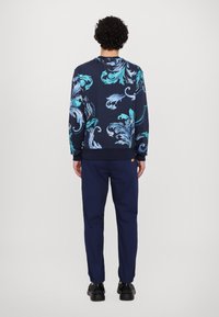 Granatowy sweatshirt z jasnoniebieskim wzorem kwiatowym, ribbowane mankiety i dół. Połączony z jednolitymi granatowymi spodniami i czarnymi butami, widok z tyłu.