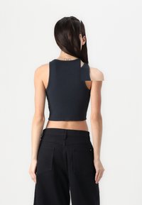 Black cropped tank top with a round neckline and sleeveless design. Paired with high-waisted black trousers featuring back pockets.
