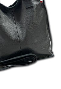 Zwarte leren handtas met een gladde textuur, zachte vorm en een lange schouderband. Bevat een kleine accent in rood en wit.