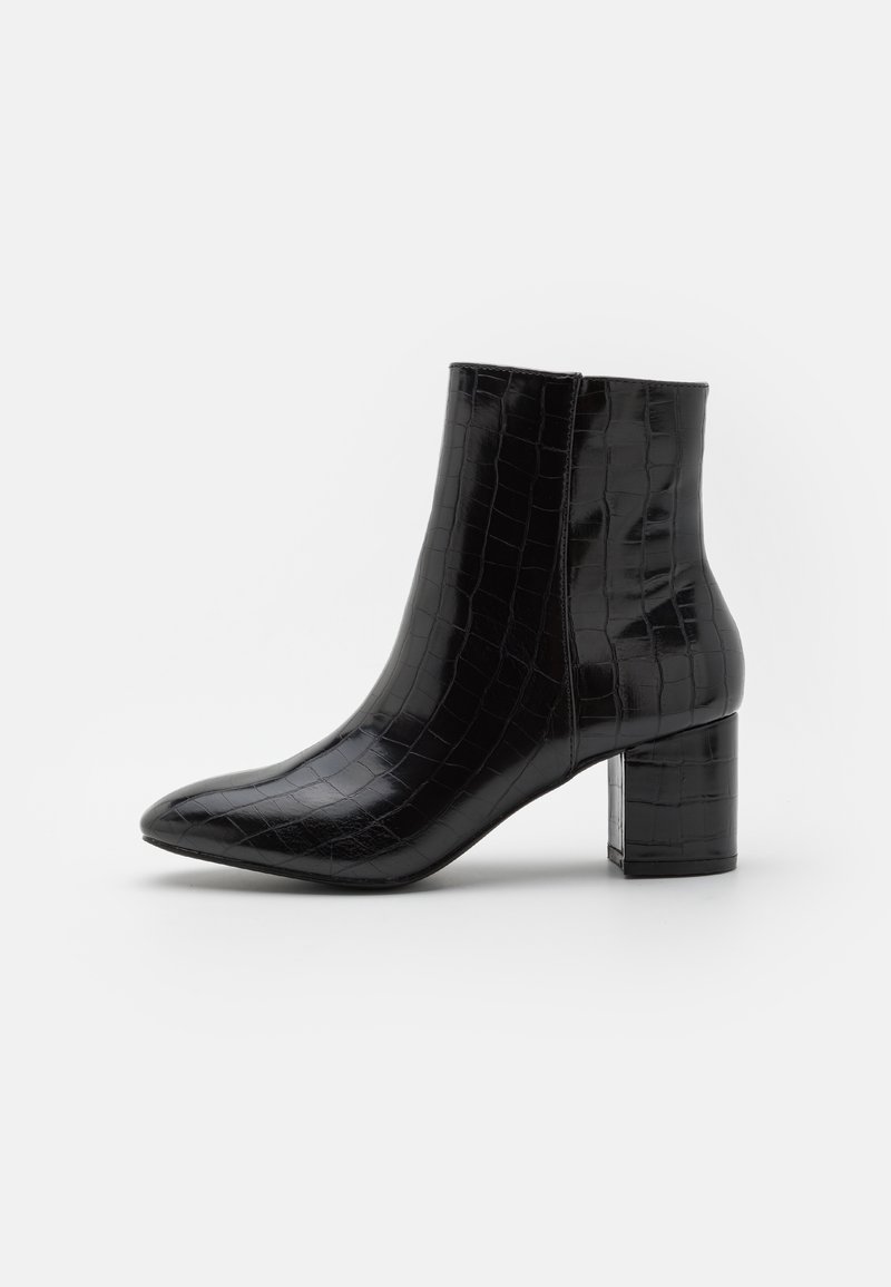 Bottes noires à la cheville en similicuir brillant à texture crocodile, avec bout pointu et talon bloc. Coutures détaillées visibles.