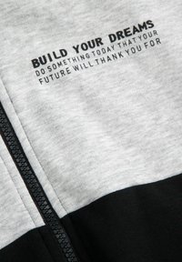 Szary i czarny materiał z czarnym zamkiem błyskawicznym i napisem "BUJ W SWOJE MARZENIA ZRÓB COŚ DZISIAJ, ZA CO TWOJA PRZYSZŁOŚĆ CI PODZIĘKUJE."