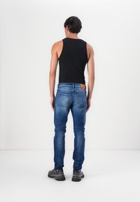 Džínsy z denimu so svetlom modrým umývaním, slim-fit strih, päť vreciek, s hnedou nášivkou na zadnej strane. Nosené s čiernym tielkom a sivými teniskami.