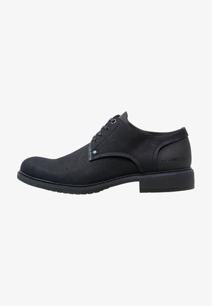 Chaussure habillée noire à profil bas avec une tige texturée, fermeture à lacets et semelle en caoutchouc. Présente des coutures discrètes et un accent de talon portant une marque.