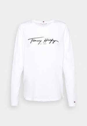 White long-sleeve T-shirt made of cotton with a round neck. Features "Tommy Hilfiger est. 1985" in black script and small logo detail on cuff.