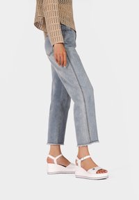 Sandali wedge bianchi con tomaia testurizzata e cinturino alla caviglia regolabile, abbinati a jeans cropped azzurri chiari con orli grezzi.