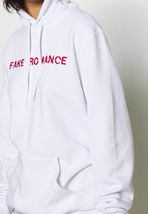 Sudadera blanca hecha de un tejido suave, con un eslogan bordado en rojo "FAKE ROMANCE" en el pecho. Incluye un bolsillo delantero tipo canguro.