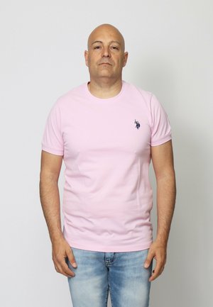 T-shirt a maniche corte color rosa con collo rotondo realizzata in cotone, caratterizzata da un piccolo logo blu navy sul lato sinistro del petto, abbinata a jeans azzurri.