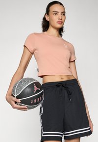 Lys rosa, kort t-skjorte med korte ermer, kombinert med svarte basketballshorts som har hvite striper og snor. Holder en basketball.