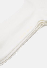 Chaussettes blanches en coton jusqu'à la cheville avec une texture côtelée et un bord élastique, comportant une étiquette de taille imprimée "CDLP 39/41" en jaune clair.